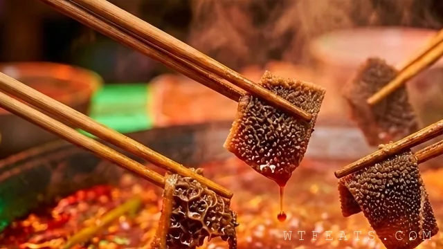 Fresh máo dù beef omasum with dark layered folds arranged like flower petals on a white plate beside a bubbling red Sichuan hot pot